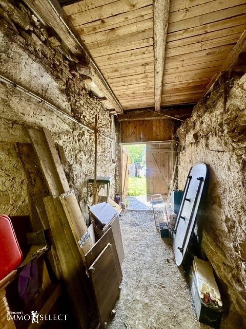 Schmaler Flur mit rauen Steinwänden und Holzdecke, der zu einem Außenbereich führt.