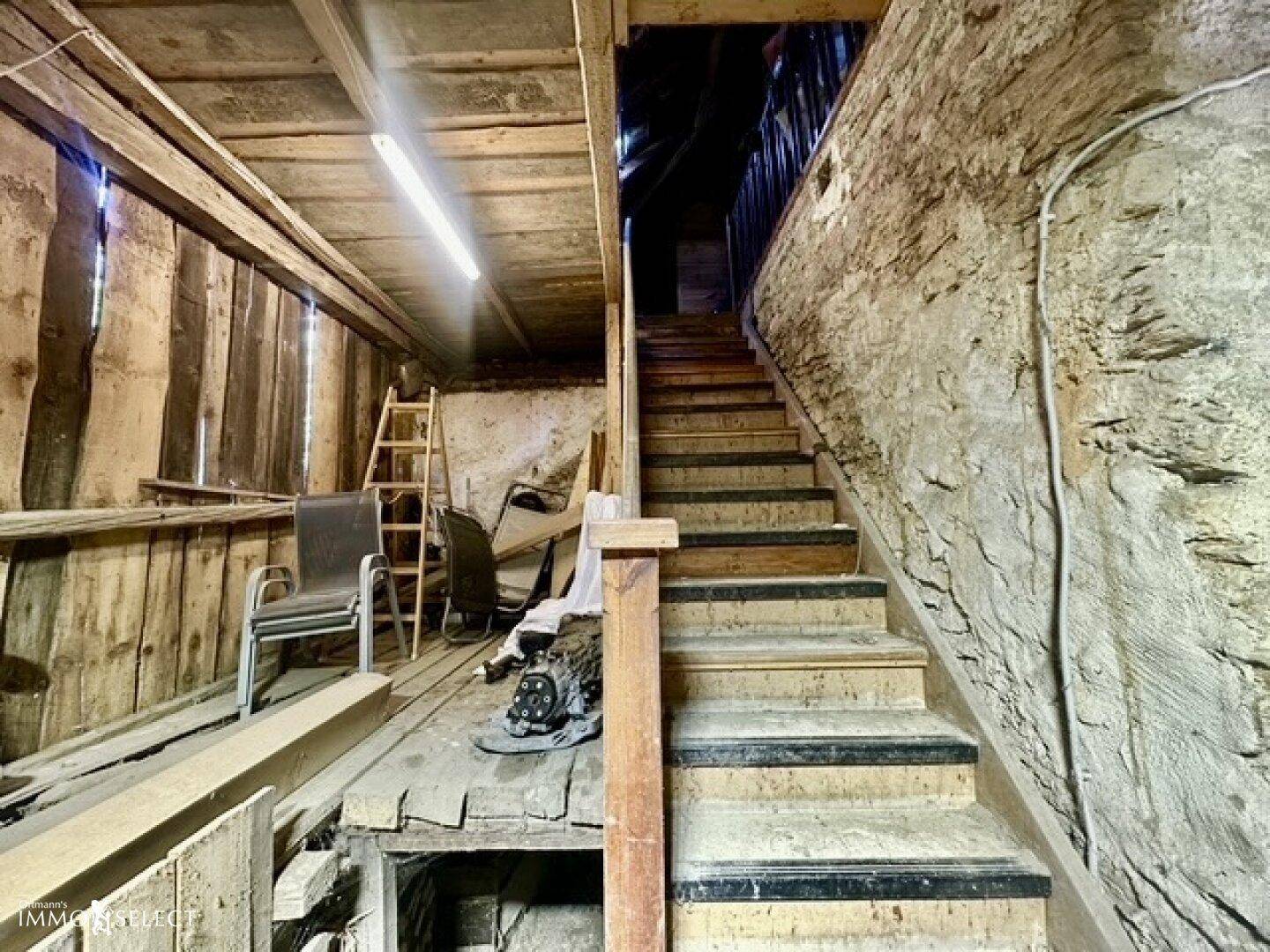 Rustikaler Treppenaufgang in einem unfertigen Bereich mit Holzwänden und Steinmauern.