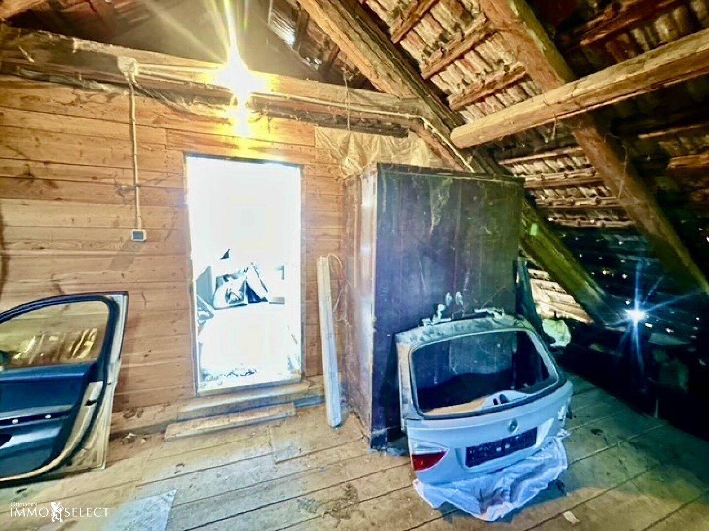 Dachbodenbereich mit Holzwänden, sichtbaren Balken und gelagerten Autoteilen.