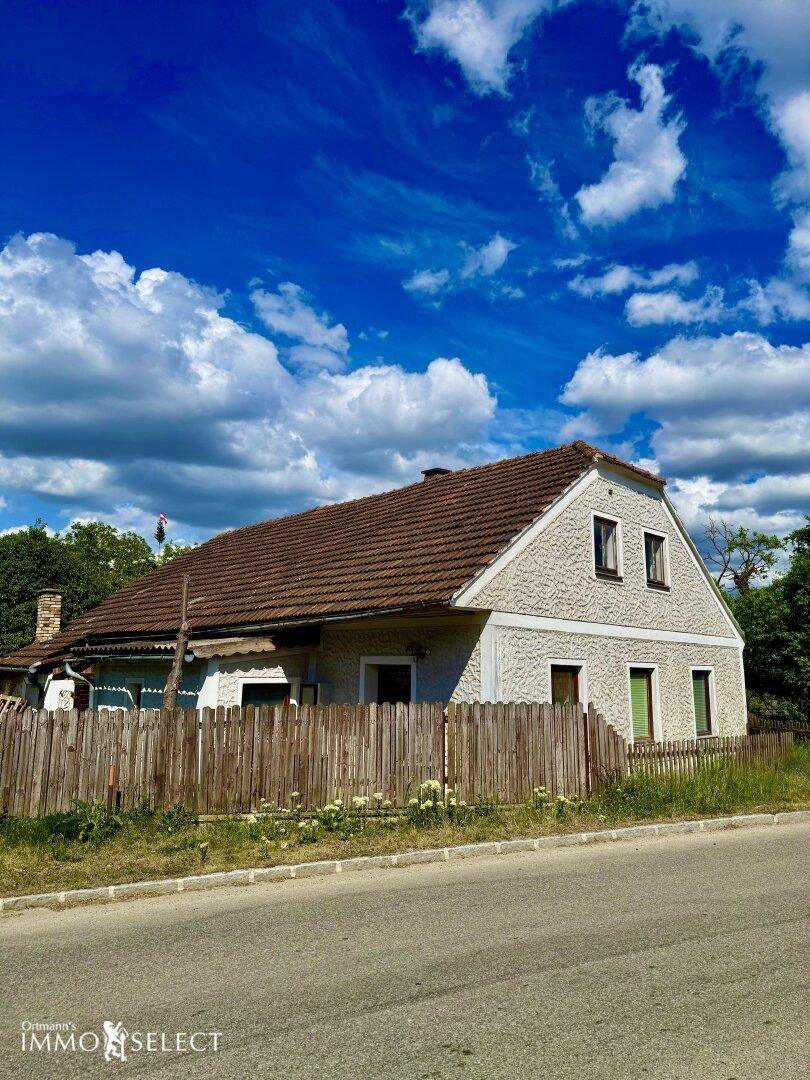 Frontansicht des Hauses von der Straße mit Ziegeldach und einem Holzzaun unter blauem Himmel.