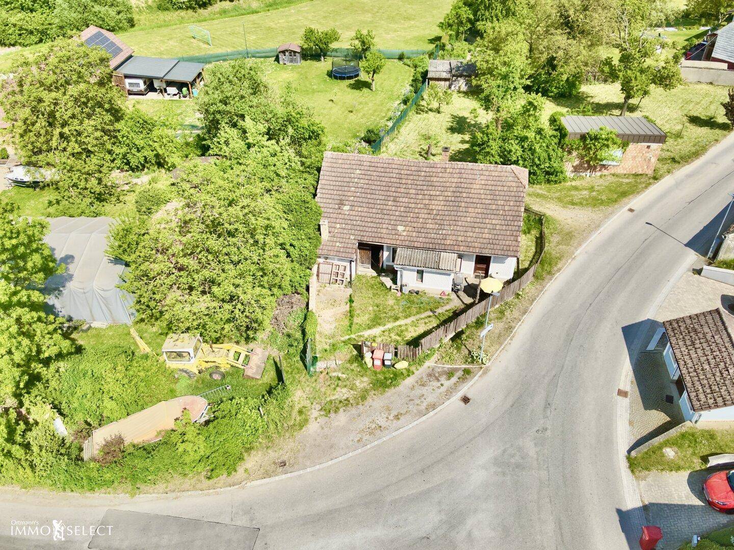 Weitläufige Luftaufnahme des Hauses in einer ländlichen Umgebung mit weiteren Gebäuden und viel Grün.