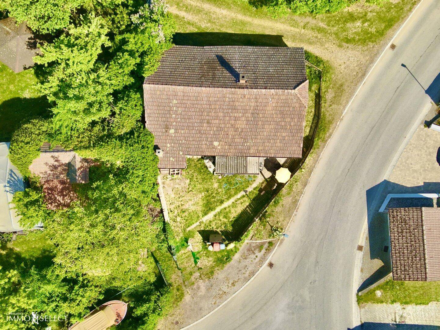 Draufsicht auf das Haus mit braunem Ziegeldach und dem umliegenden Grundstück mit Gartenbereich und Straße.