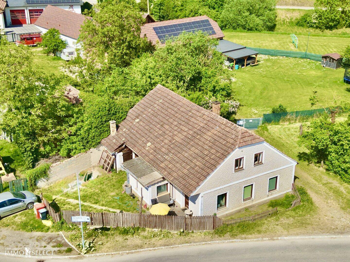 Luftaufnahme des Hauses mit Ziegeldach, umgeben von grüner Natur und einem geparkten Auto.
