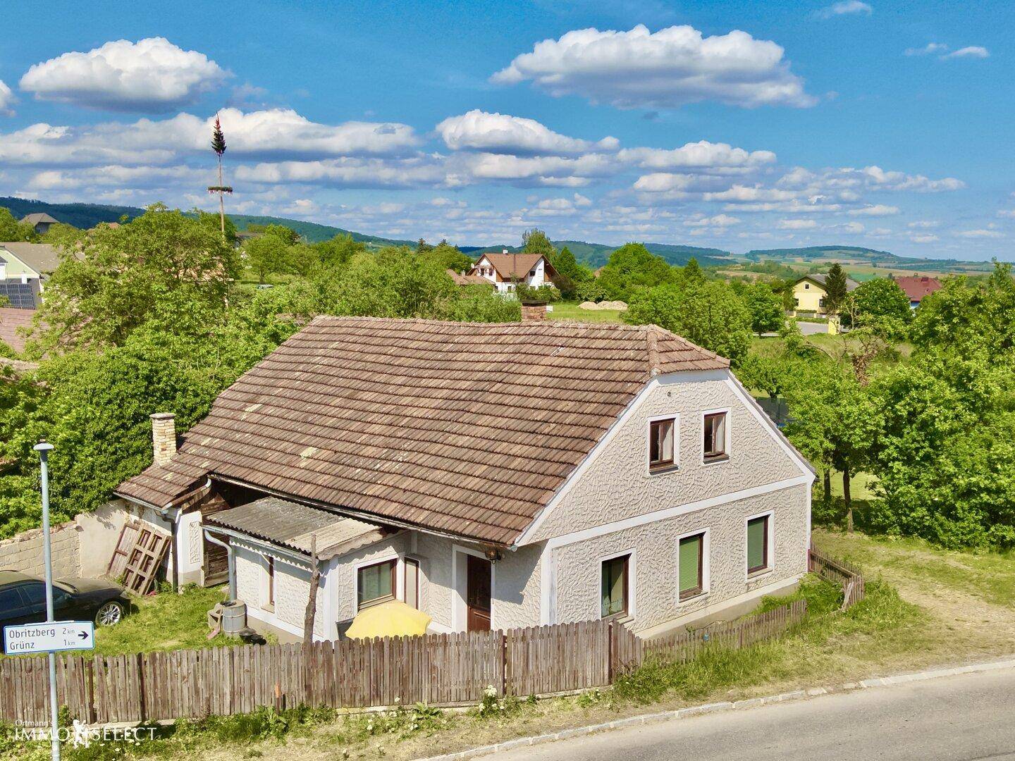 Freistehendes Haus mit braunem Ziegeldach und heller Fassade, umgeben von viel Grün in einer ruhigen Landschaft.