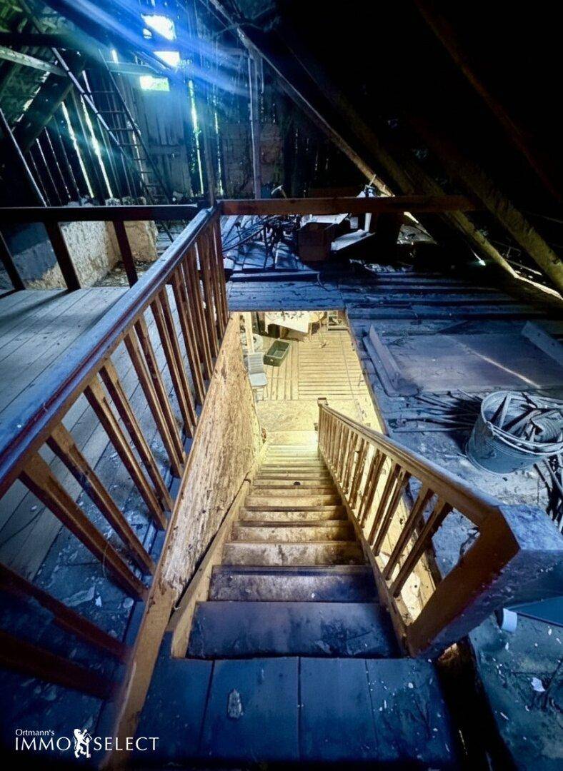 Blick von oben auf eine Holztreppe in einen unfertigen Dachbodenbereich mit Holzbalken.