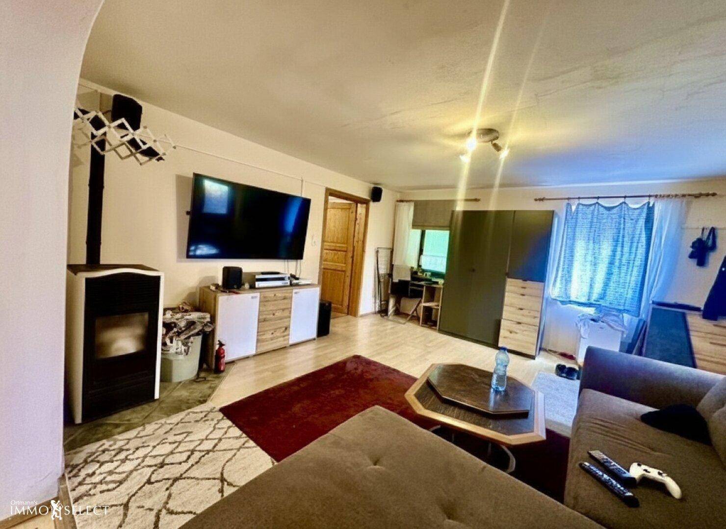 Heller Wohnraum mit großem Fernseher, gemütlichem Holzofen und Holzboden.