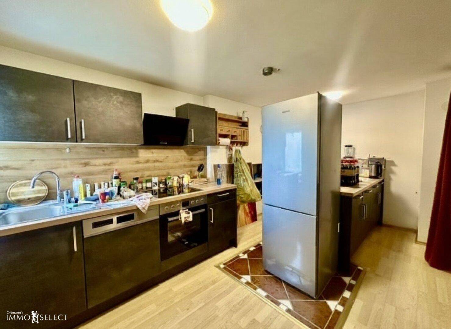 Funktionale Küche mit dunklen Schränken, integriertem Herd und großem Kühlschrank.
