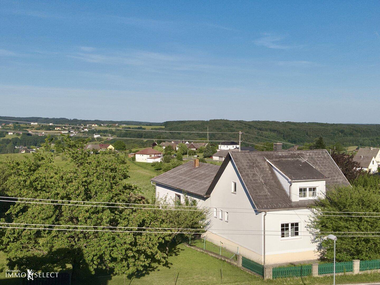 Seitenansicht des Hauses aus der Luft, mit Satteldach und weitem Blick über die grüne Landschaft.