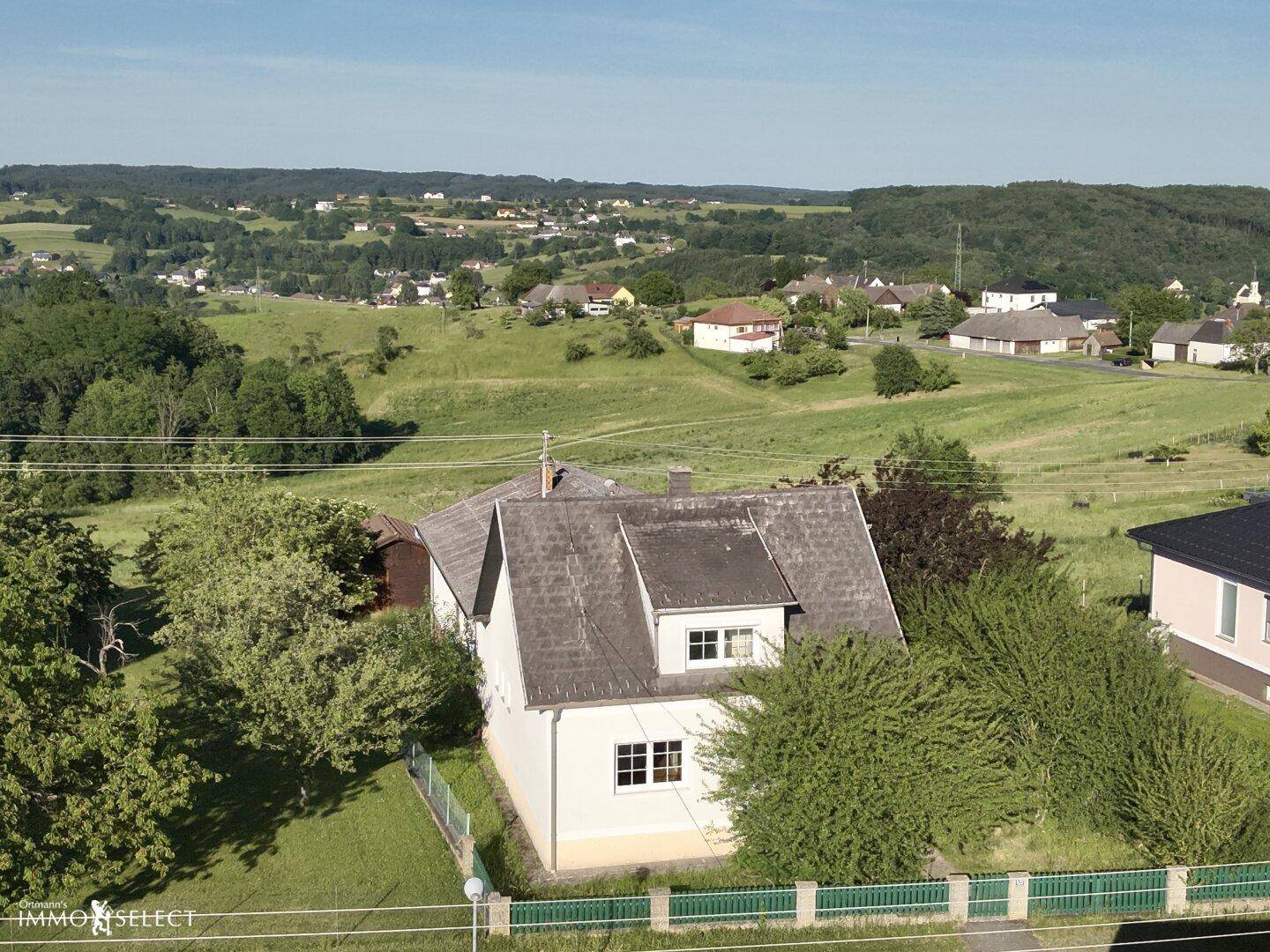 Luftaufnahme eines Hauses in ländlicher Umgebung mit weitem Blick über grüne Hügel und Felder.