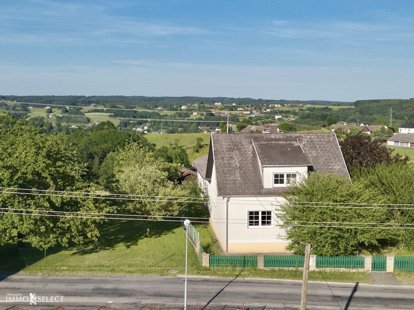 Seitenansicht des Hauses aus der Luft, mit Satteldach und weitem Blick über die grüne Landschaft.