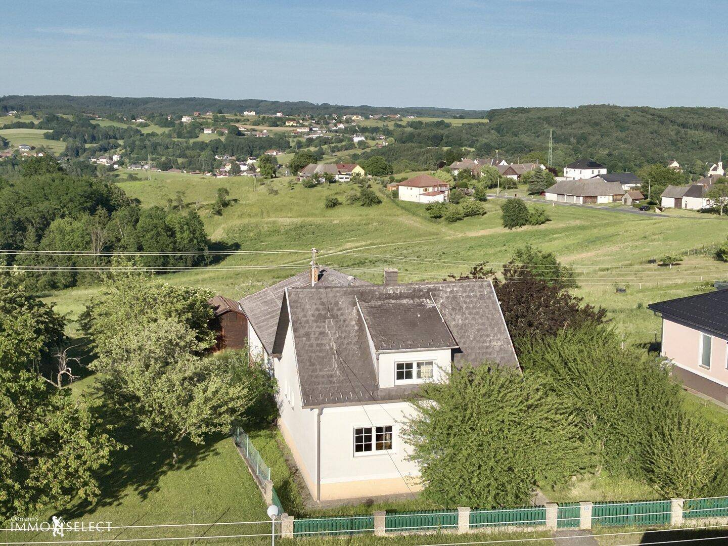 Luftaufnahme eines Einfamilienhauses mit Satteldach und Blick auf die hügelige, grüne Landschaft.