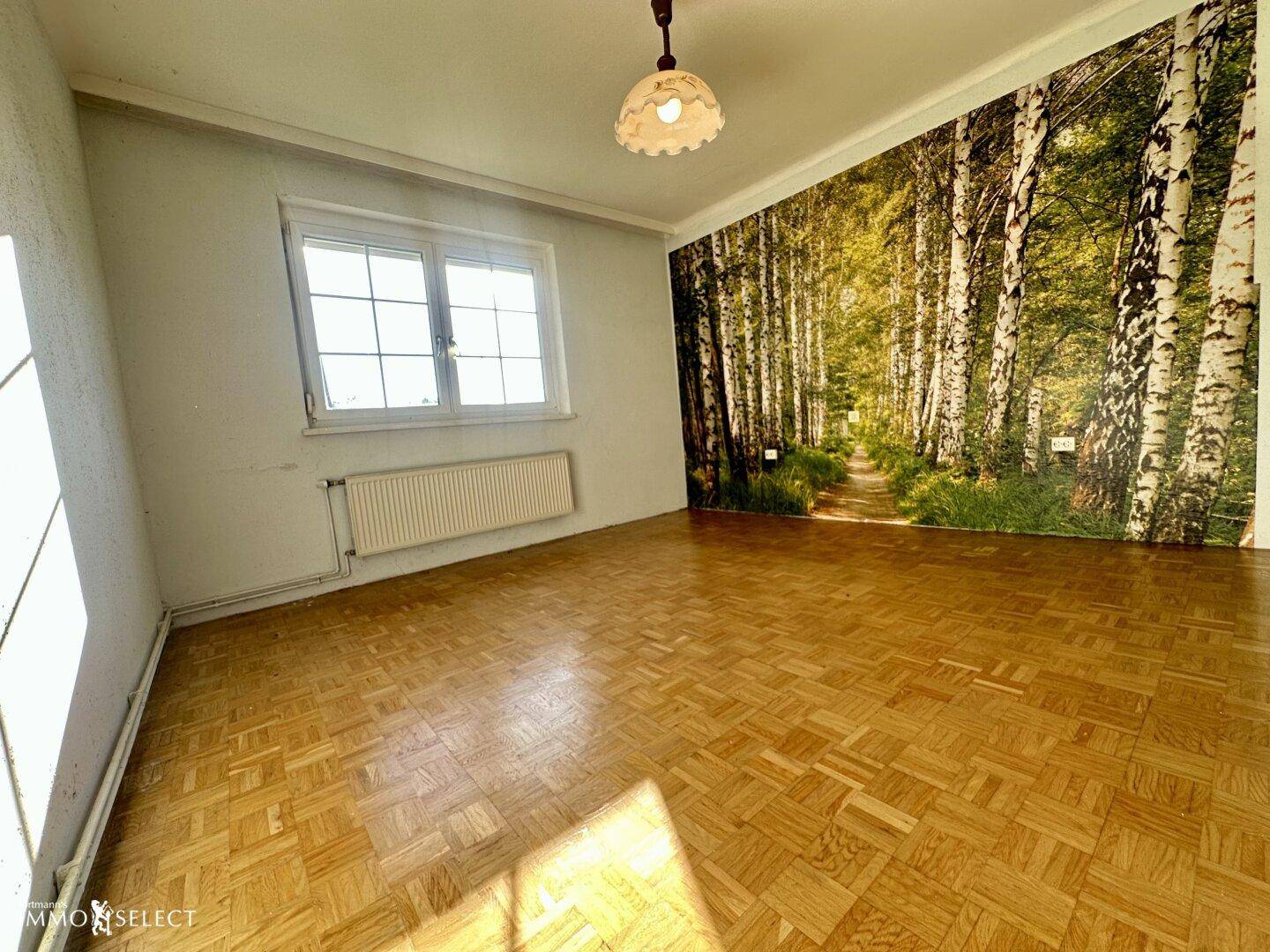Geräumiges Zimmer mit Fischgrätparkett, einer Waldtapete und viel natürlichem Licht.