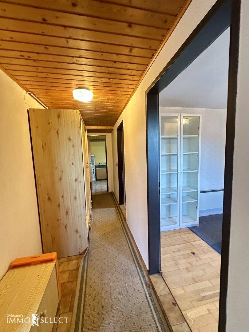 Langer Flur mit Holzdecke und Teppichboden, der verschiedene Räume miteinander verbindet.