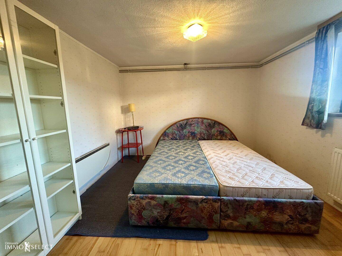 Schlafzimmer mit Doppelbett, Regal und Fenster, das Tageslicht hereinlässt.