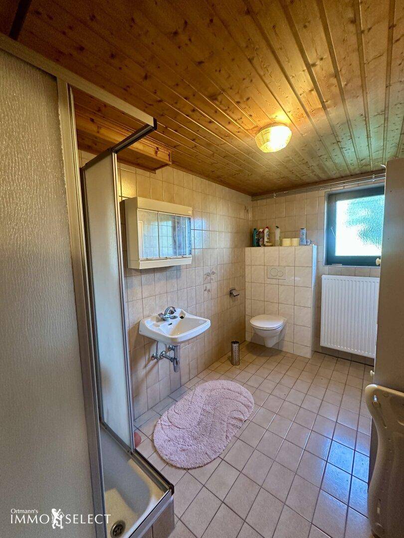 Badezimmer mit Duschkabine, Waschbecken und WC, ausgestattet mit Fliesen und Holzdecke.