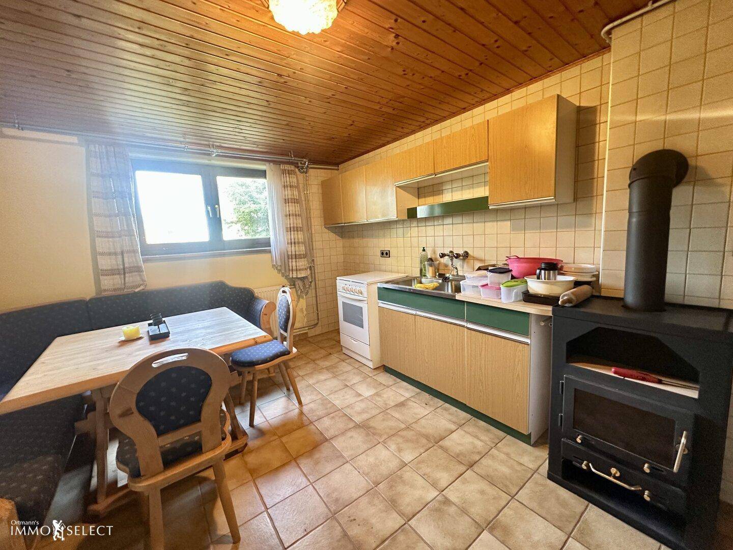 Funktionale Küche mit Holzschränken, Essbereich und einem traditionellen Holzofen.