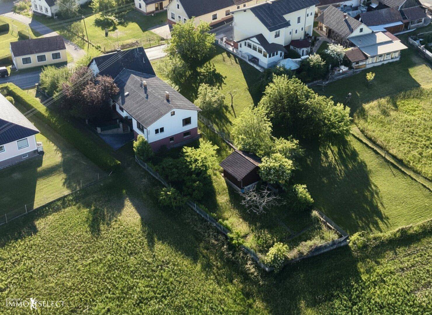 Weitläufige Luftaufnahme einer ländlichen Siedlung mit Wohnhäusern, Gärten und weiten Grünflächen.