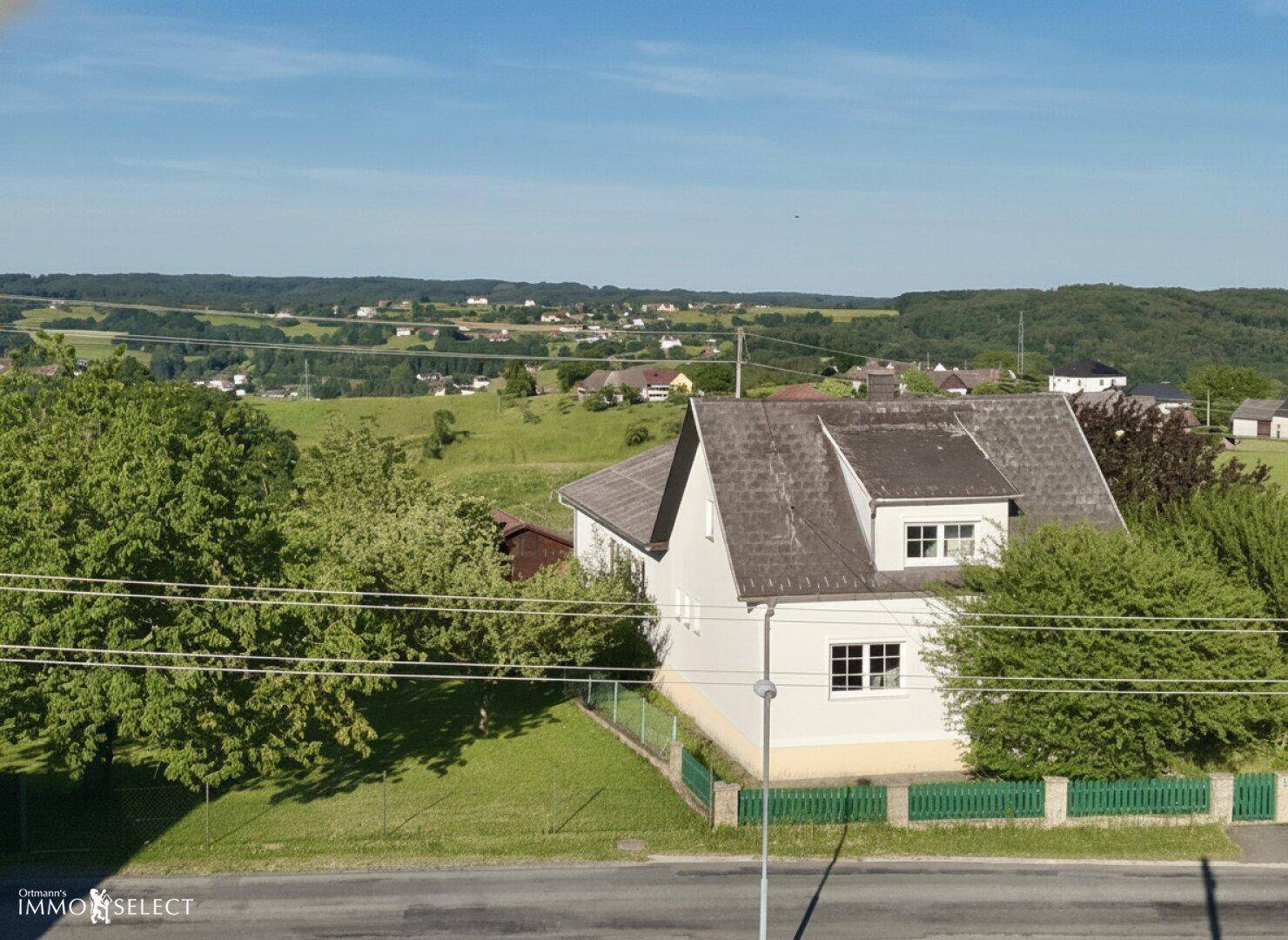 Panoramablick auf ein Wohnhaus in einer idyllischen Landschaft mit weiten grünen Feldern und Wäldern.