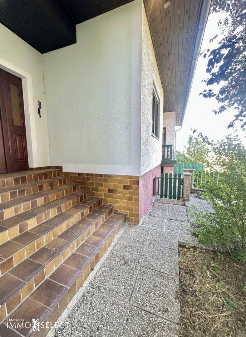 Eingangsbereich des Hauses mit gefliesten Stufen, einer braunen Tür und einem kleinen Gehweg.