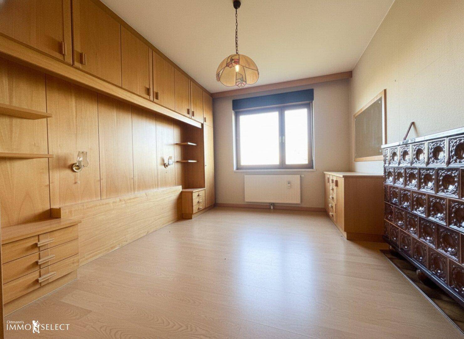 Schlafzimmer mit Holzeinbauschränken, Parkettboden und einem traditionellen Kachelofen als Heizelement.