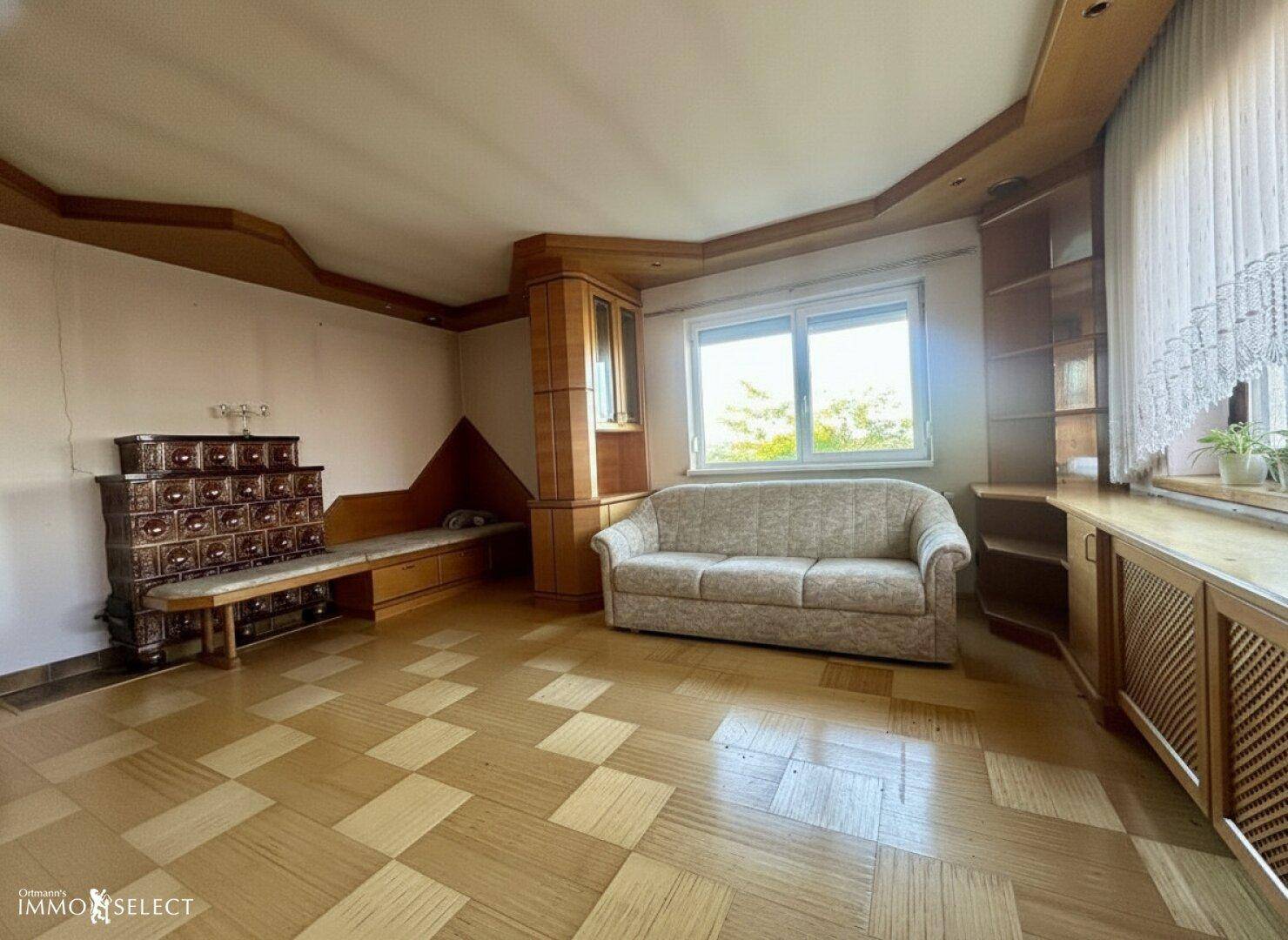 Gemütliches Wohnzimmer mit Kachelofen, Sofa und Holzvertäfelung, die eine warme Atmosphäre schafft.