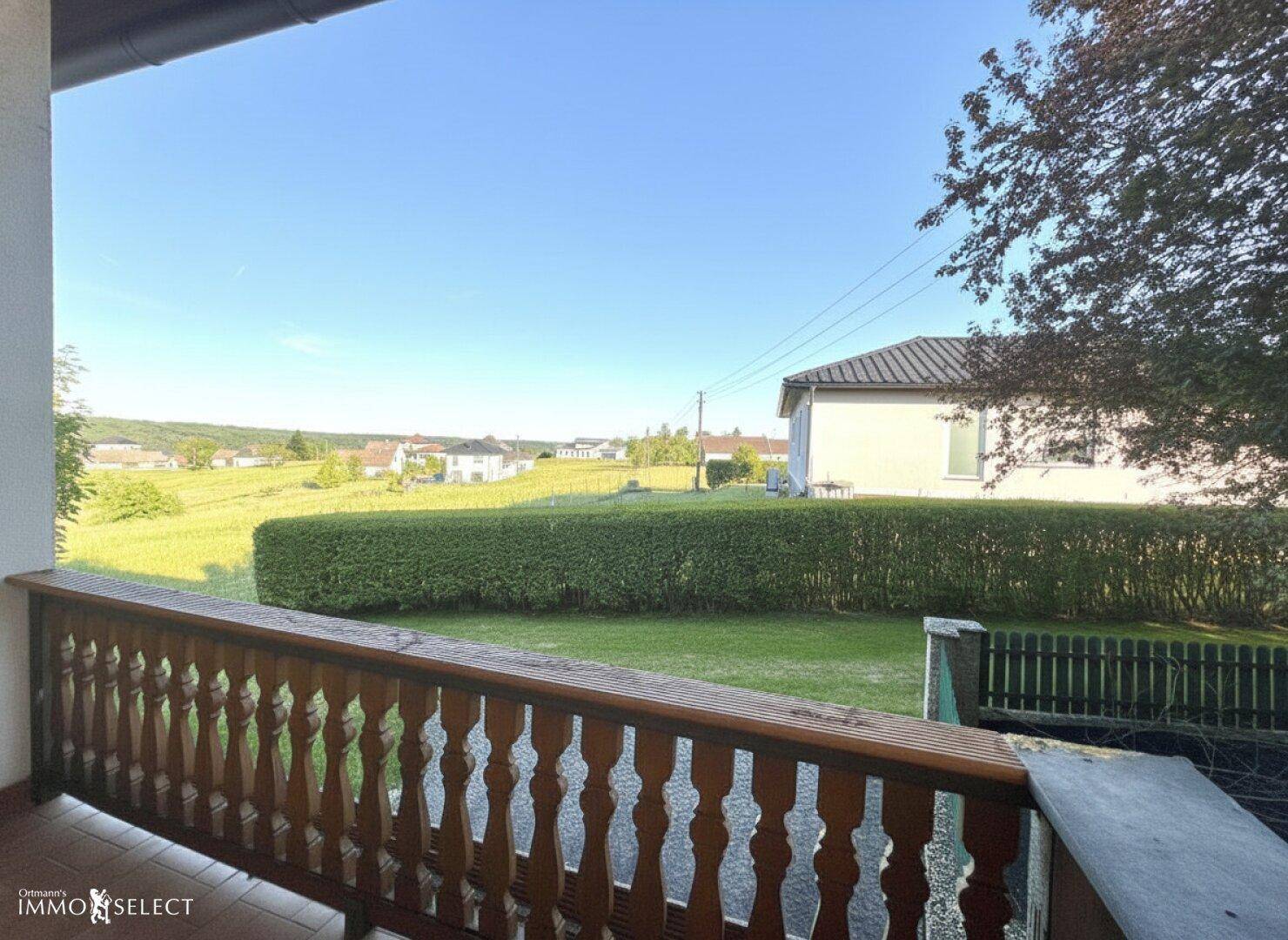Balkon mit weitem Blick über die grüne Landschaft und eine gepflegte Hecke im Vordergrund.