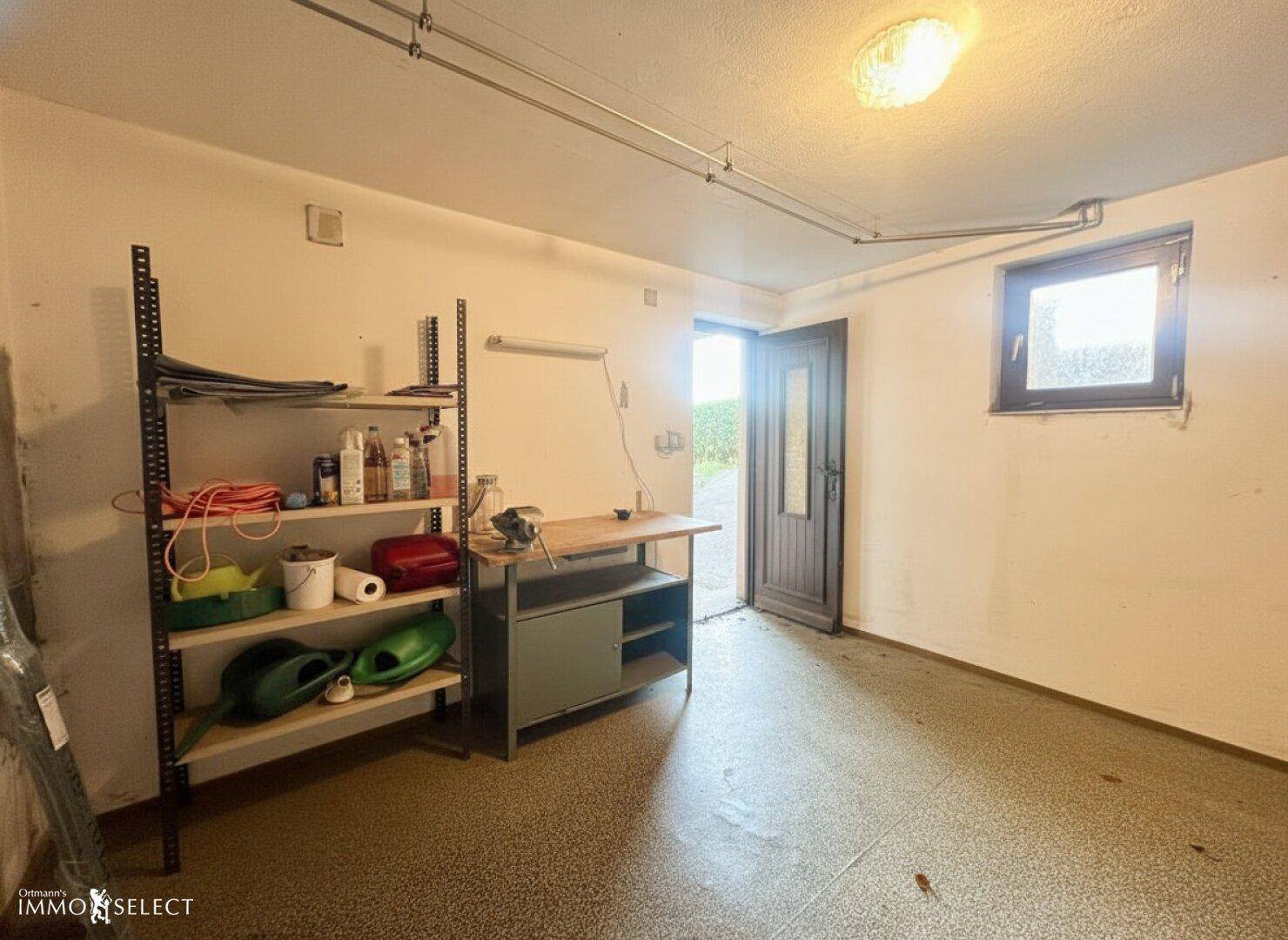 Werkstatt oder Abstellraum mit Regalen, Werkbank und Fenster, das Tageslicht hereinlässt.