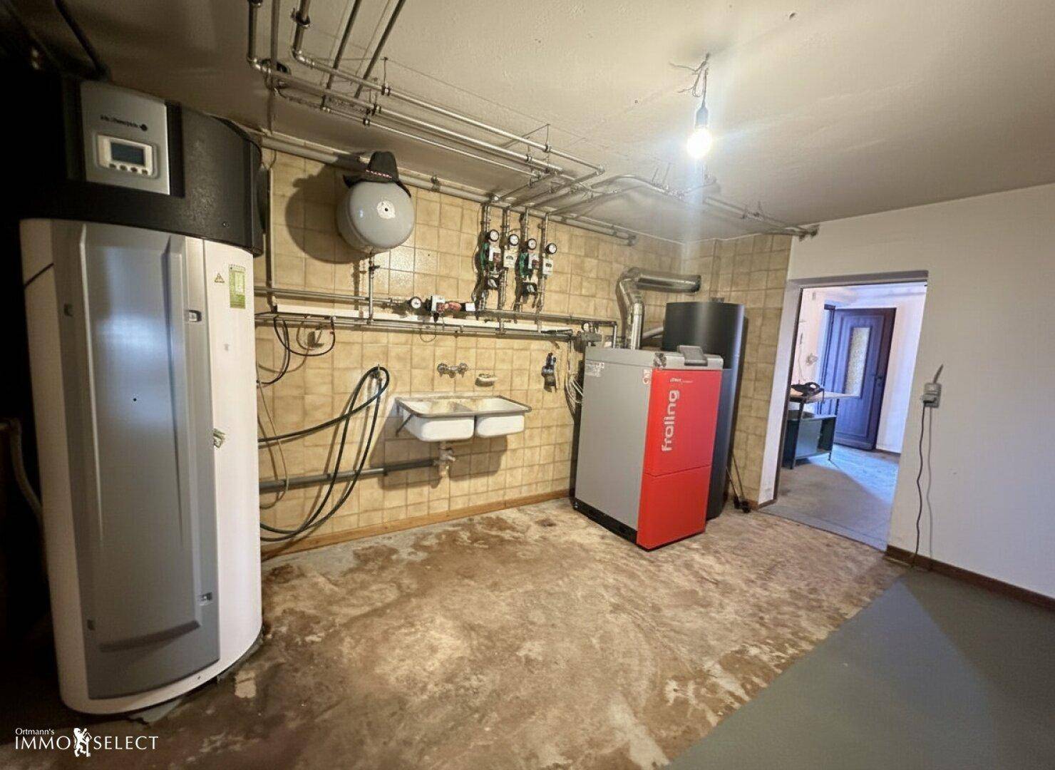 Heizungsraum mit moderner Pelletheizung und Warmwasserspeicher, umgeben von Fliesenwänden.