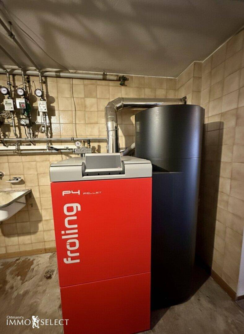 Detailansicht einer modernen Pelletheizung im Heizungsraum, umgeben von Fliesenwänden.