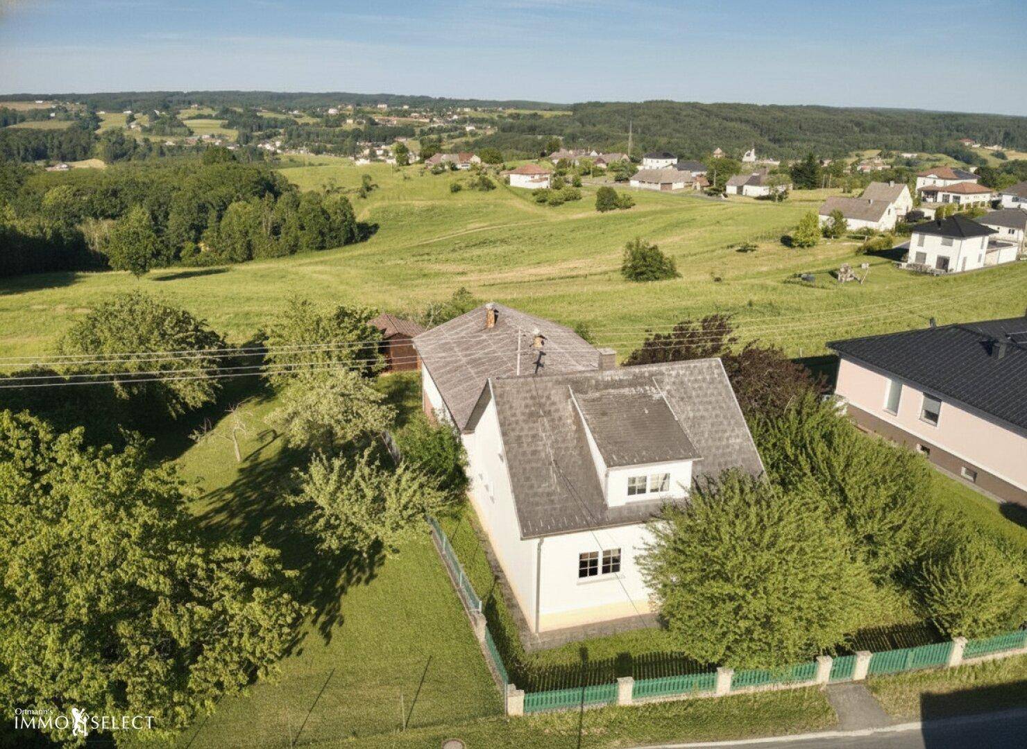 Luftaufnahme eines Hauses in ländlicher Umgebung mit weitem Blick über grüne Hügel und Felder.