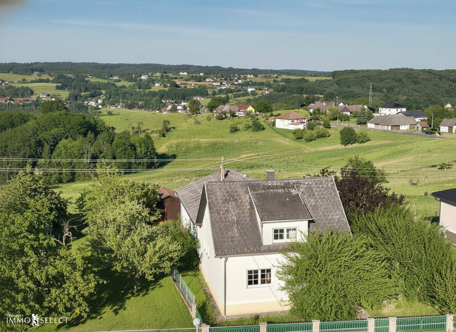 Luftaufnahme eines Hauses in ländlicher Umgebung mit weitem Blick über grüne Hügel und Felder.