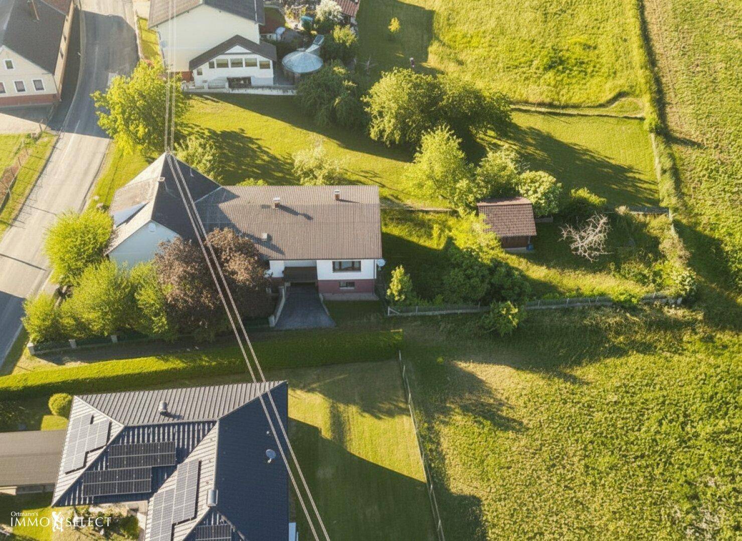 Weitläufige Luftaufnahme des Anwesens mit angrenzenden Feldern und einem Nachbarhaus mit Photovoltaikanlage.