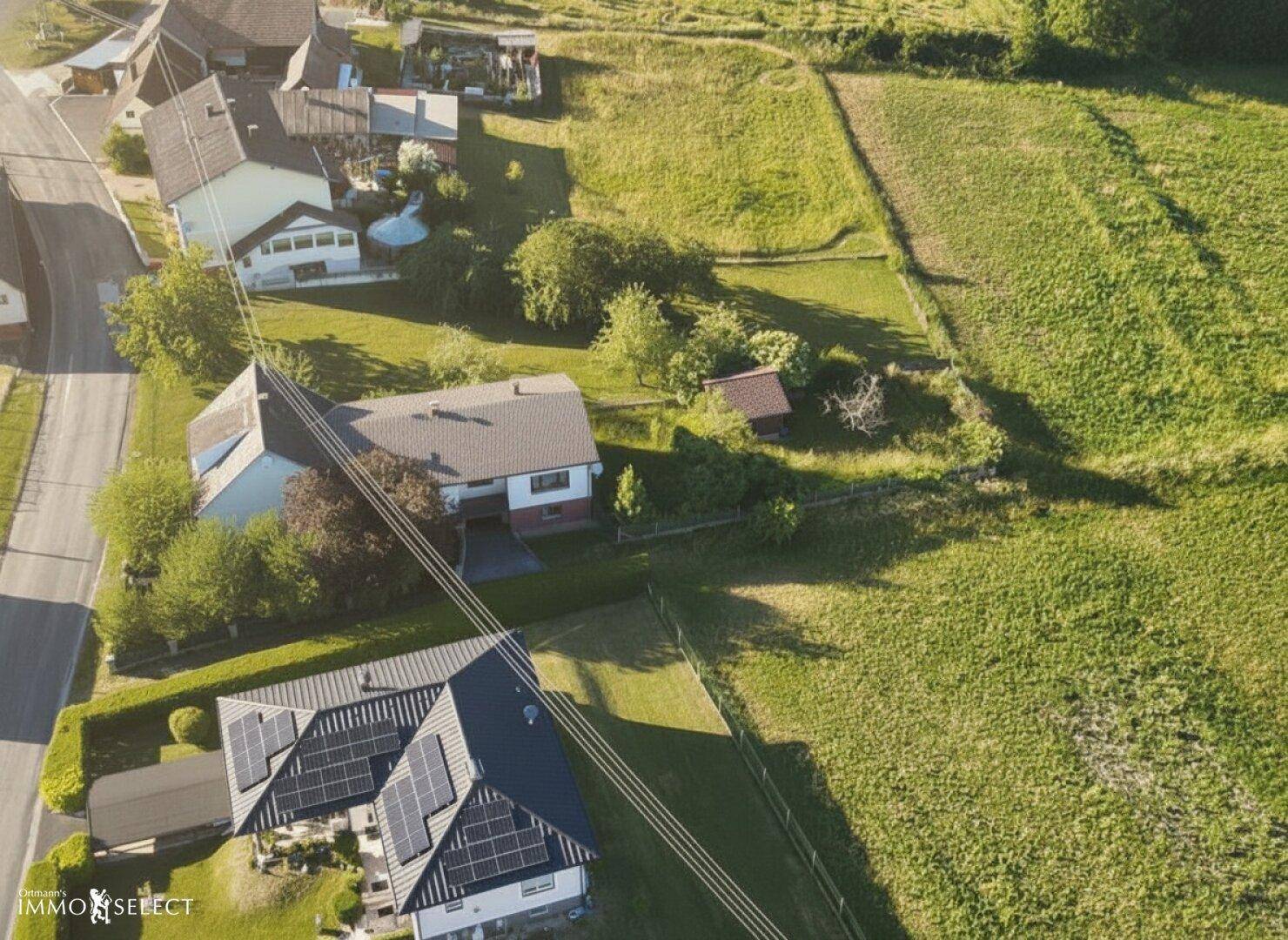 Weitläufige Luftaufnahme des Anwesens mit angrenzenden Feldern und einem Nachbarhaus mit Photovoltaikanlage.
