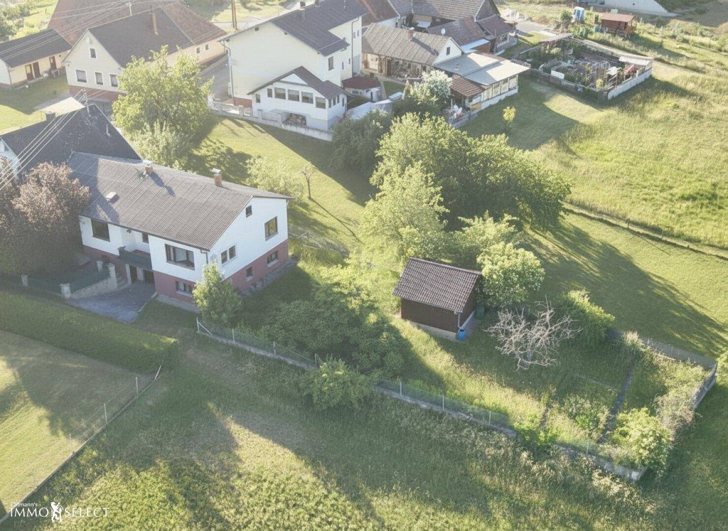 Luftaufnahme eines Wohnhauses mit angrenzendem Garten und weiteren Häusern in der ländlichen Umgebung.
