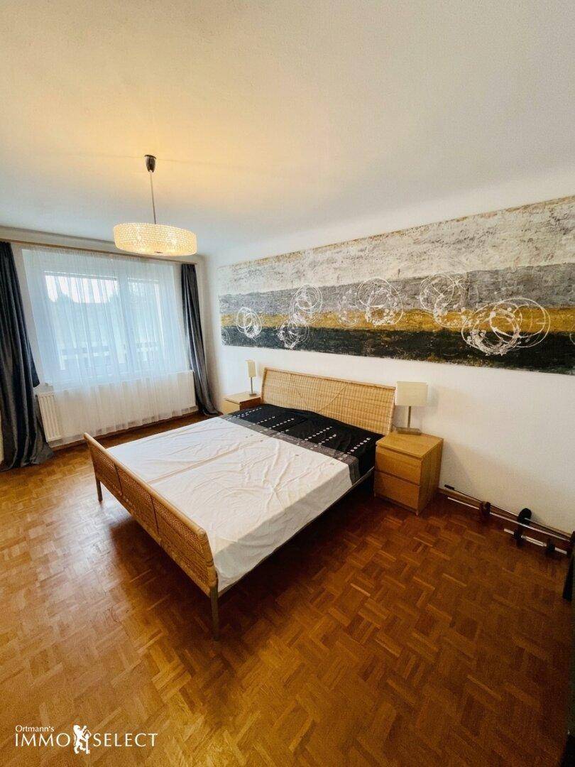 Helles Schlafzimmer mit Parkettboden, großem Bett und dekorativer Wandkunst über dem Kopfteil.