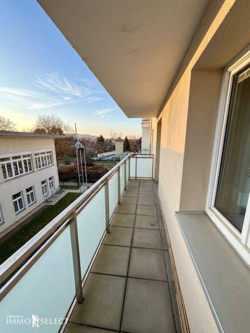 Langer, schmaler Balkon mit Glasgeländer und Blick auf die Umgebung, ideal für frische Luft.