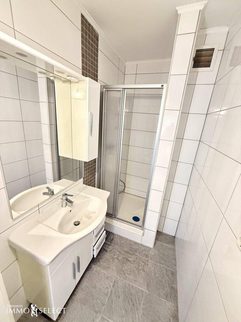 Modernisiertes Badezimmer mit Duschkabine, Waschtisch und weißen Fliesen.