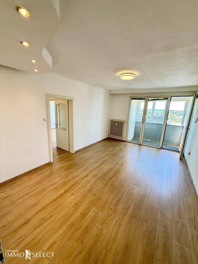 Geräumiges Wohnzimmer mit Laminatboden, Deckenstrahlern und Zugang zum Balkon.