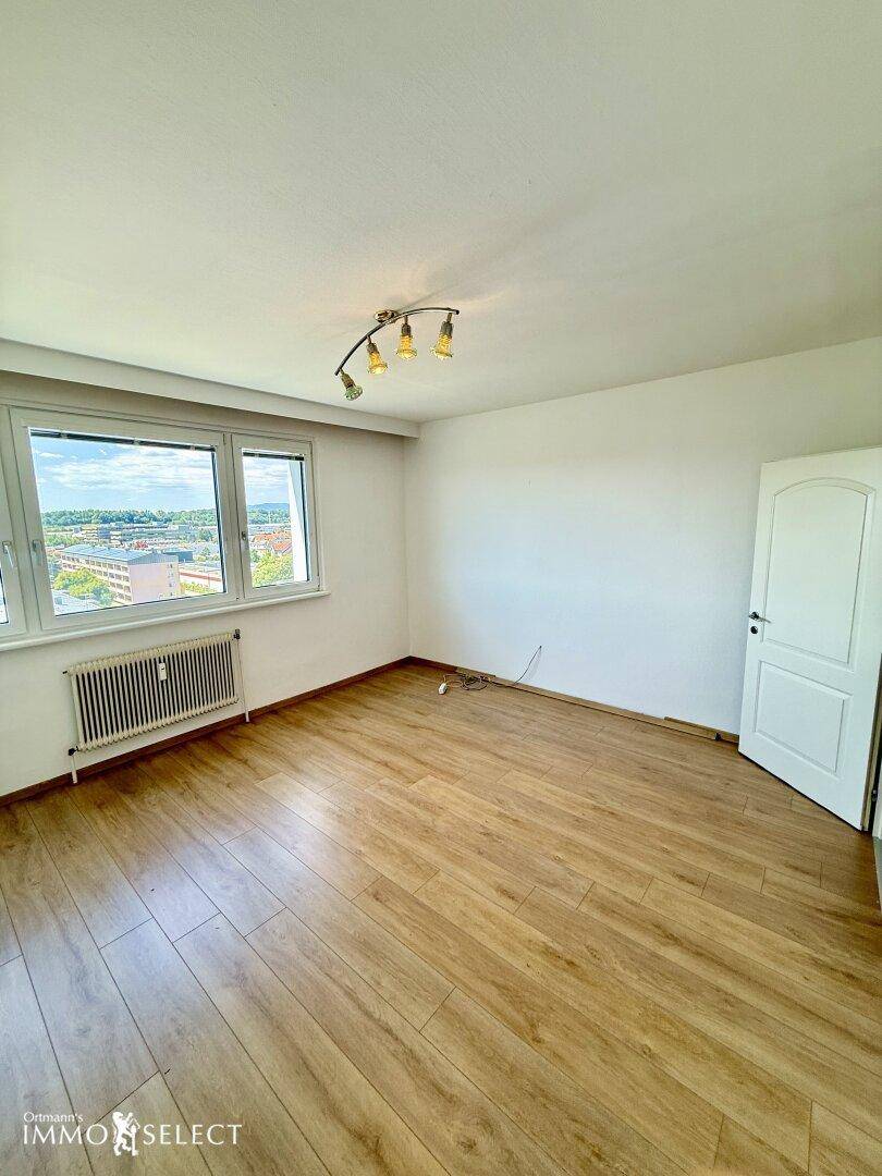 Helles Schlafzimmer mit Laminatboden, großem Fenster und Heizkörper.