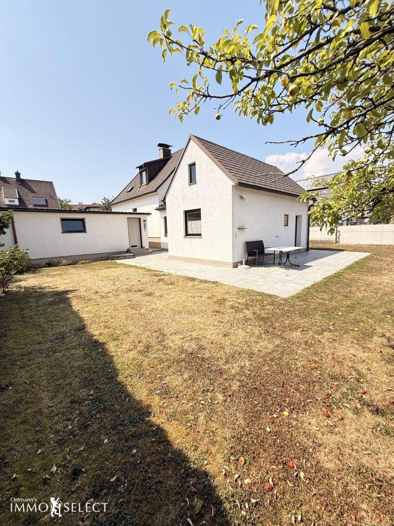 Rückansicht des Hauses mit einer gepflasterten Terrasse und einem weitläufigen Gartenbereich.