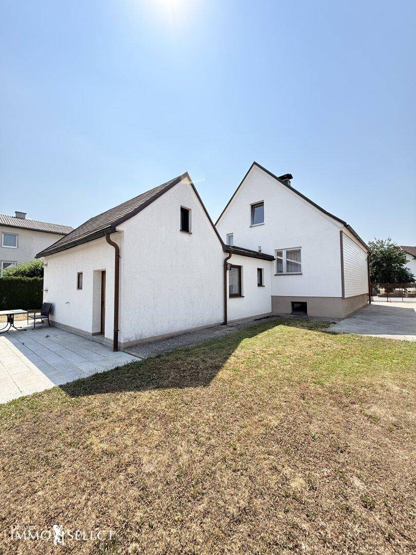 Seitenansicht des Hauses mit Anbau und einem weitläufigen, sonnigen Gartenbereich.
