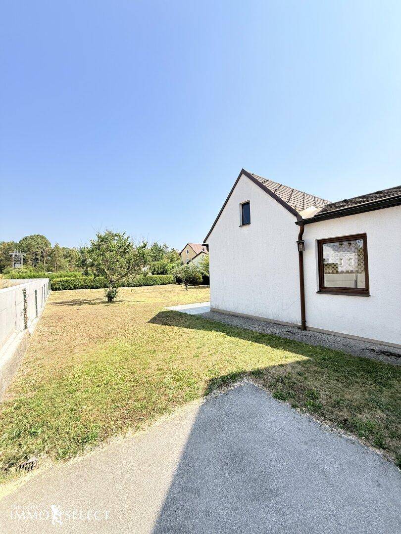 Seitenansicht des Hauses mit einem gepflegten Gartenweg und weitläufiger Rasenfläche unter blauem Himmel.