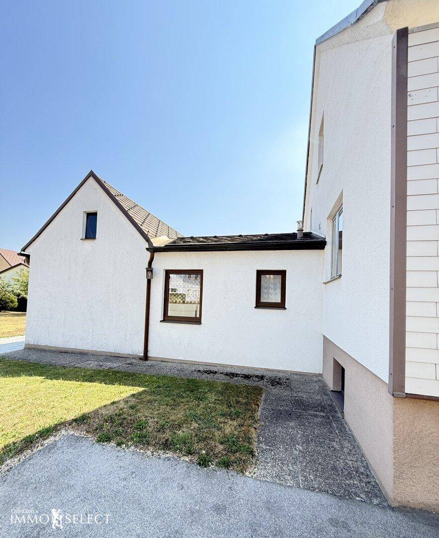 Schmaler Durchgang zwischen zwei Gebäudeteilen des Hauses, mit seitlichem Grünstreifen.