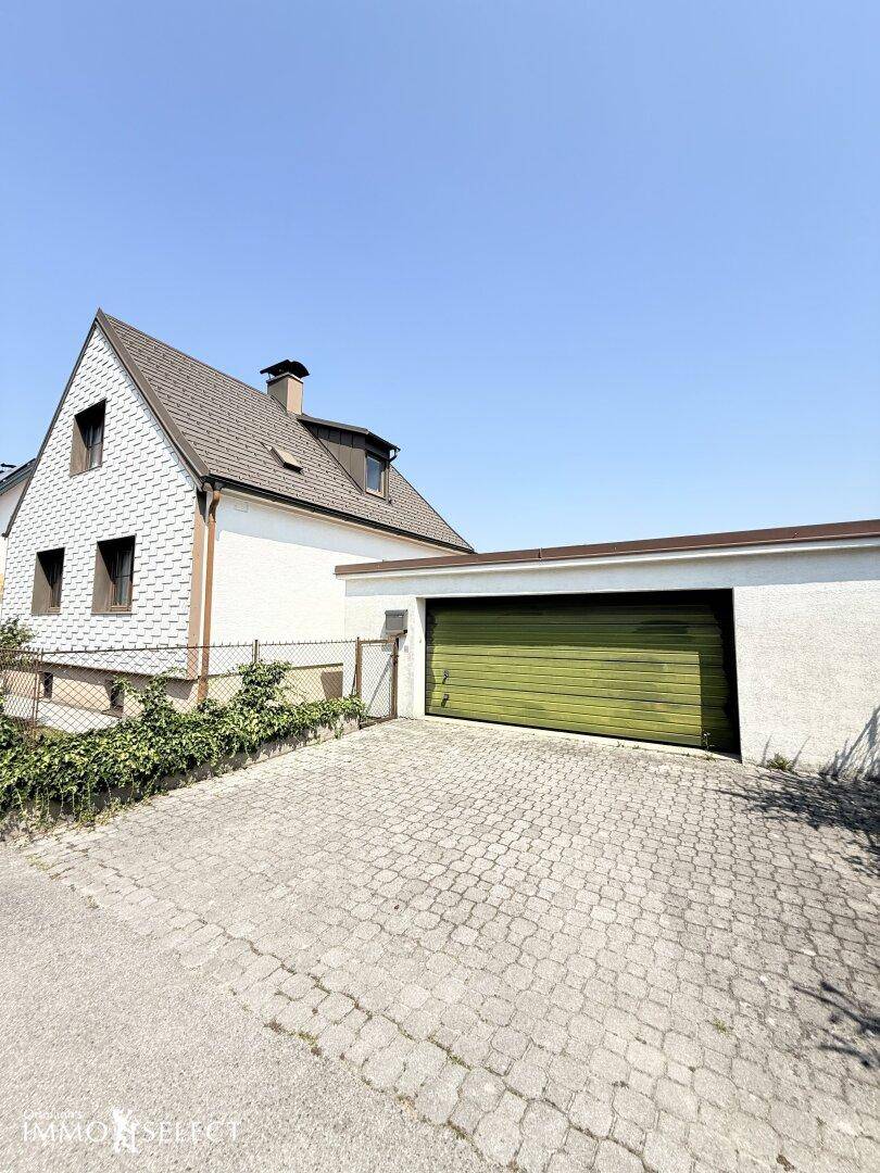 Garage mit grünem Tor und gepflasterter Zufahrt, angrenzend an das Wohnhaus unter blauem Himmel.