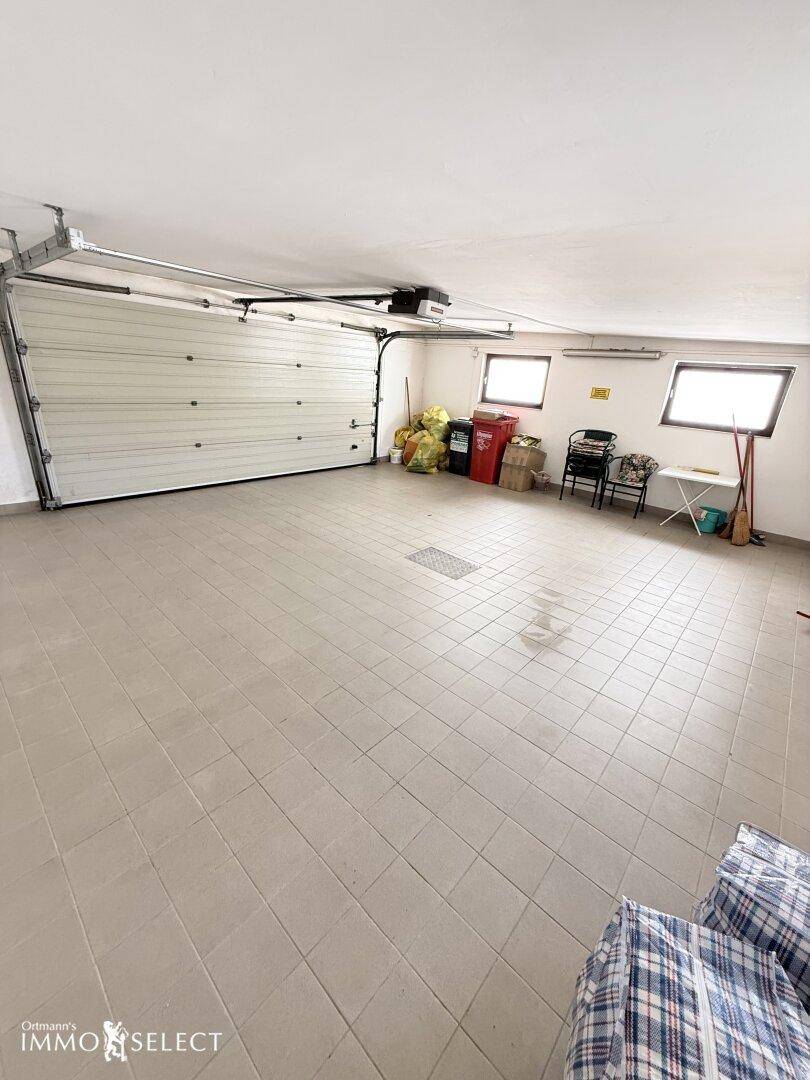 Geräumige Garage mit Fliesenboden, Rolltor und ausreichend Platz für Fahrzeuge und Lagerung.