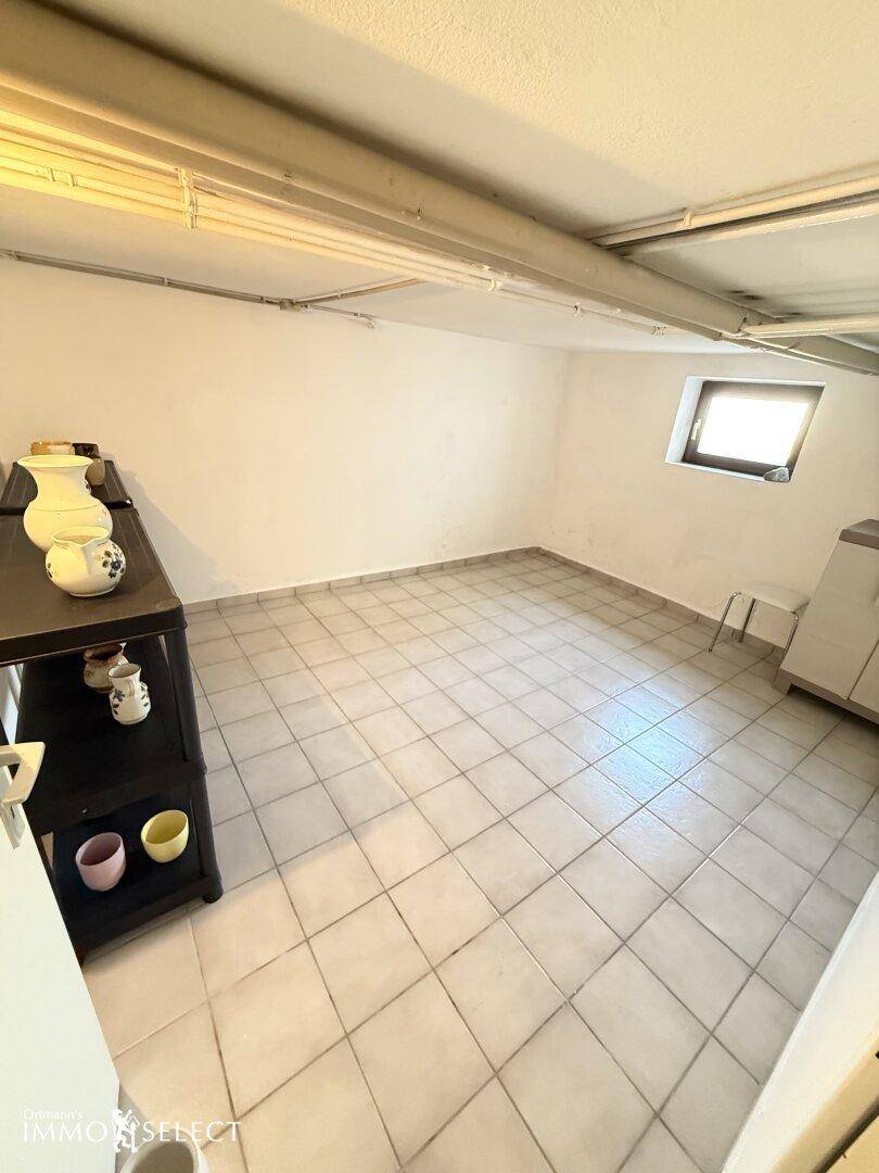 Heller Kellerraum mit Fliesenboden, kleinem Fenster und praktischen Regalen für zusätzlichen Stauraum.