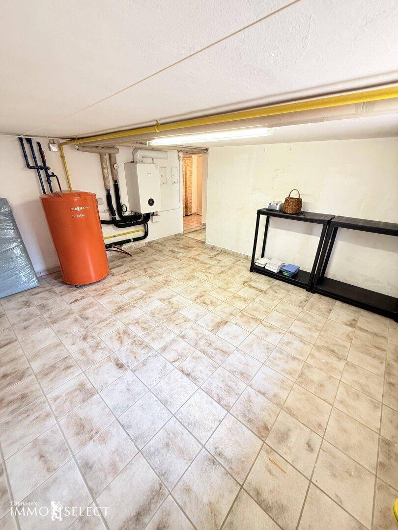 Technikraum im Keller mit Warmwasserspeicher, Heizungsanlage und robustem Fliesenboden.