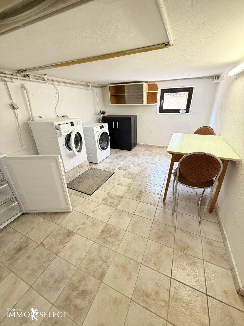 Waschküche im Keller mit Waschmaschinen, einem Tisch und praktischem Fliesenboden.