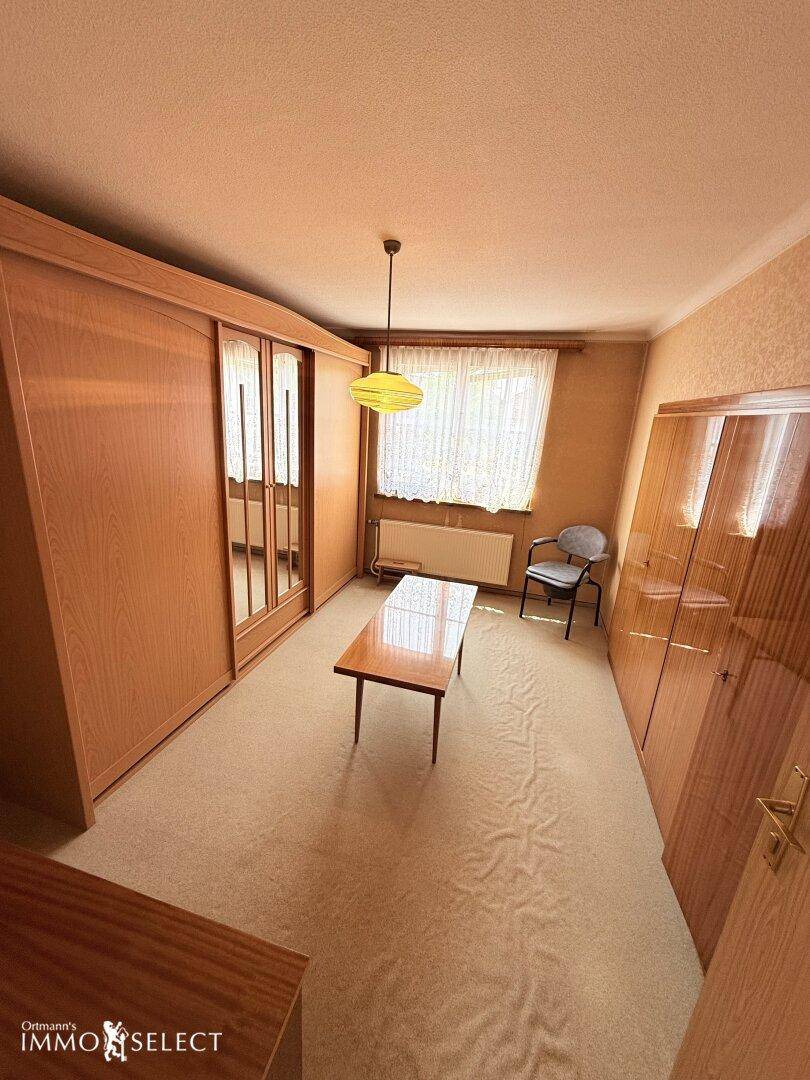 Schlafzimmer mit großem Holzschrank, Spiegeltüren und Teppichboden, hell beleuchtet durch ein Fenster.