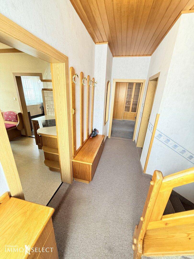 Heller Flur mit Teppichboden, Holzdecke und einer Garderobe aus Holz für den Eingangsbereich.